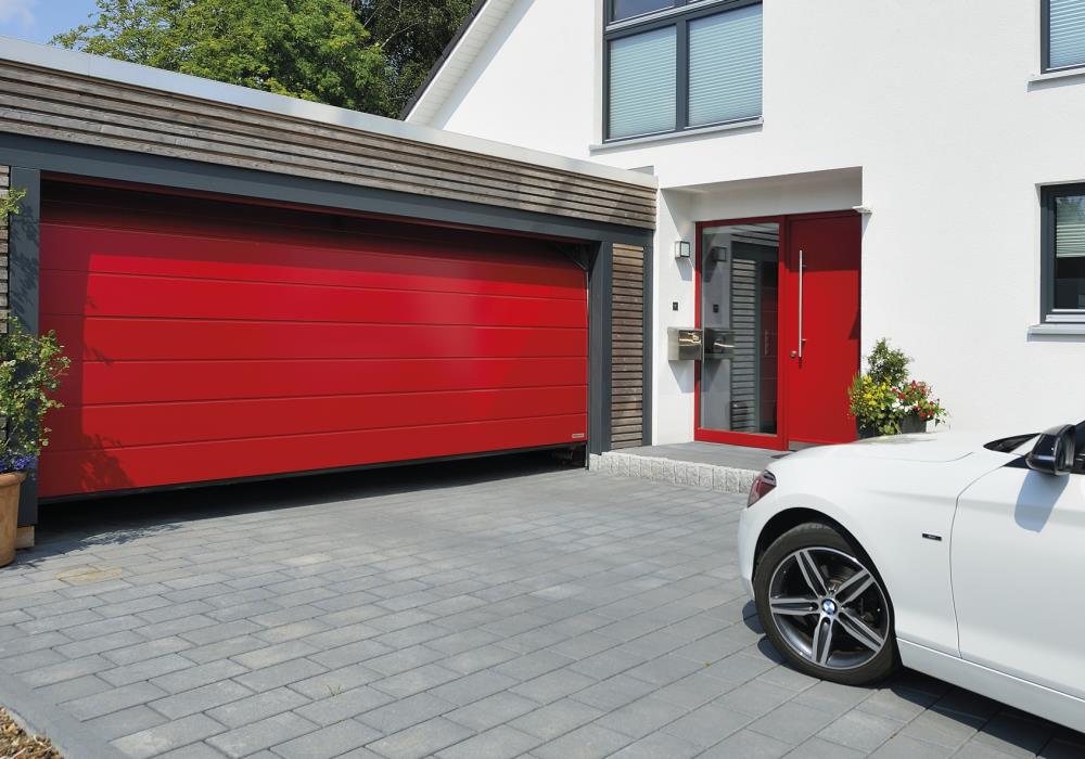 Puerta de garaje roja con coche blanco y puerta peatonal.